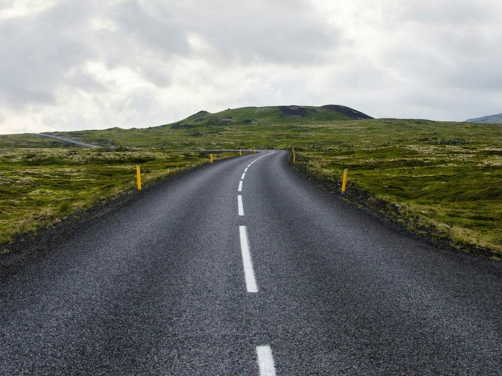 An empty road stretching through green open countryside towards distant hills